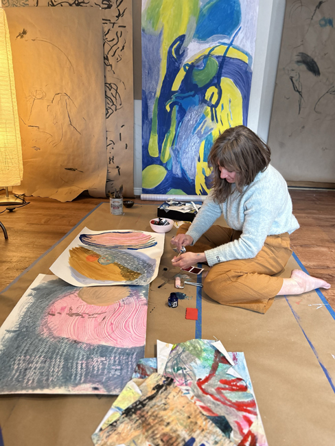 Wren Ross paints while seated on the ground 