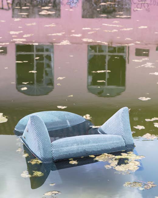 Photograph of a blue velvet chair partially submerged in water.