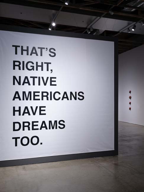 Installation view of Language in Times of Miscommunication, with a white panel that reads "That's right, Native Americans have dreams too," in bold san serif font in black letters