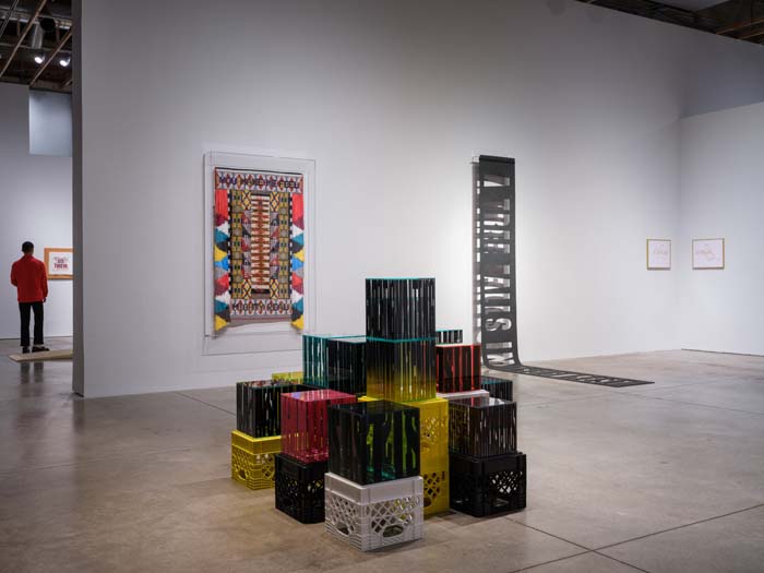 Installation view of Language in times of Miscommunication, with a series of stacked colored boxes with printed, elongated words in the foreground