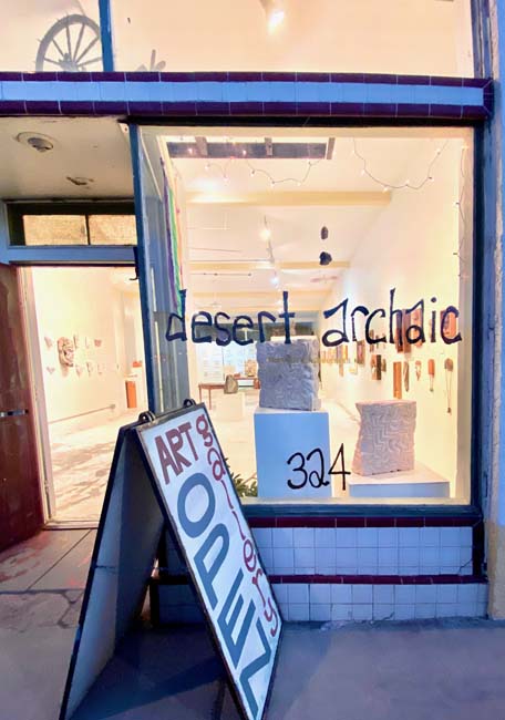 Storefront of Desert Archaic with lit windows and a sandwich board outside that reads "Art Open"