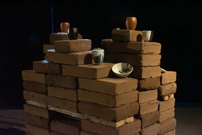 Stacks of adobe bricks with ceramic vessels at varying heights.