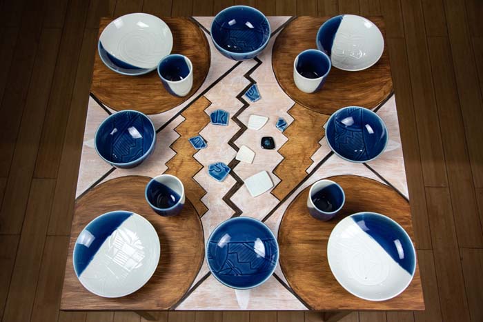 View from above over a table setting with white and blue porcelain ware and a geometric circles and zig-zag pattern painted on a wood table.