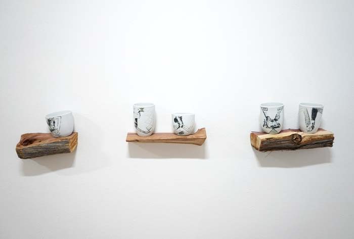 Three short rough-hewn wooden shelves holding white porcelain cups.