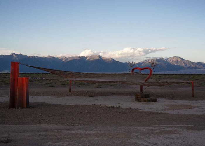 Large red hammock sculpture with heart-shaped supports, with the Collegiate Peaks of Colorado in the background.