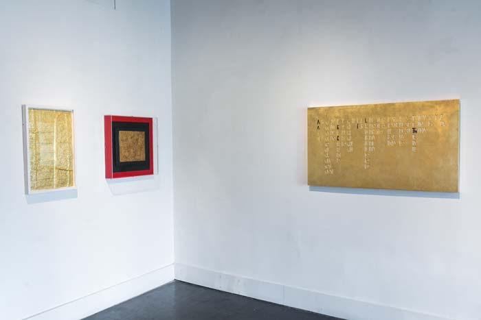 Installation view of I am Not Your Mexican, with three two-dimensional works hung in a corner, all sharing a common color of gold, with one piece framed in black and red.