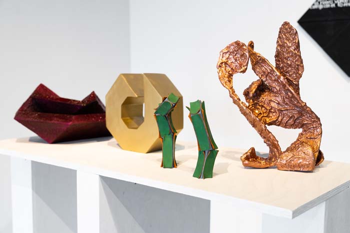 Installation view of I am Not Your Mexican featuring four small-scale sculptures by Hersúa on a white shelf.