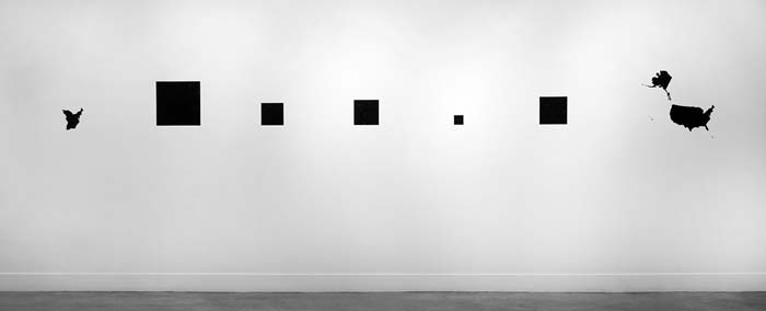 Five squares of black ink of varying sizes on a white wall.