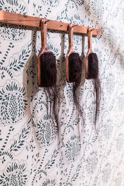 A trio of hairbrushes hanging by their handles with brown hair dangling out of them.