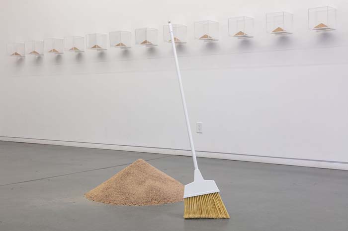 A broom standing next to a pile of sand on the floor.