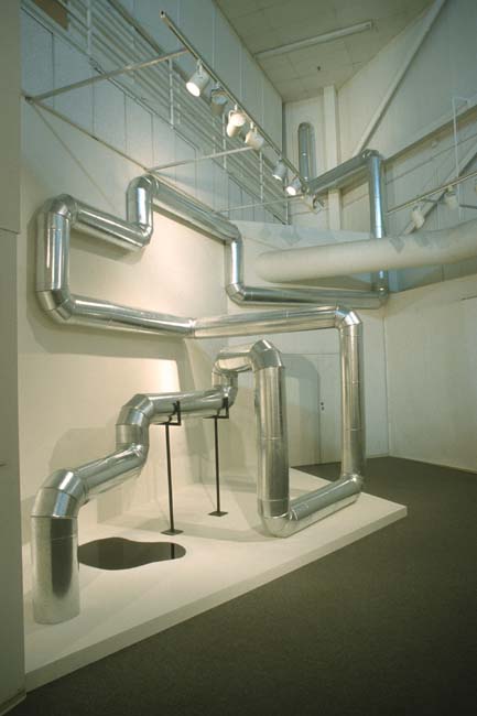 A silver pipe bending and snaking geometrically through an interior space.