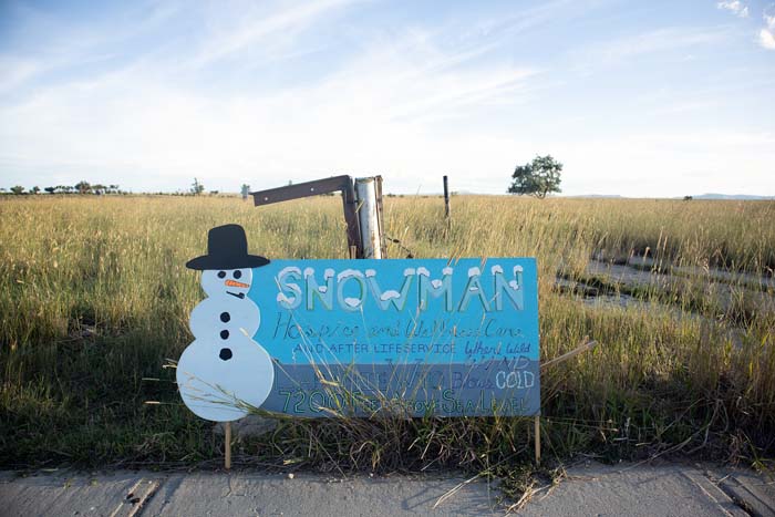 A blue hand-painted sign with a picture of a snowman and the words "Snowman Hospice and Wellness Care".