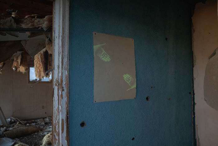 A screen print on kitakata paper depicting a pair of hands that glow in the dark, installed on a wall of an abandoned house in Shirley Basin, Wyoming.