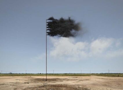 A still from a computer-simulated video of a flag puffing thick black smoke against a clear bright sky on the site where the world first struck oil, in Texas.