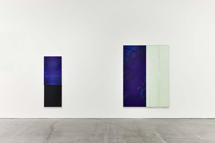 Installation view of a gallery with two artworks: on the left, a long, vertical dark blue monochromatic canvas; and on right, a diptych with the left side the same dark blue, and the right a monochromatic off-white.