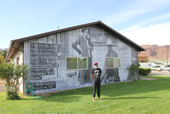 Chip Thomas poses in front of a mural of historic Moab rancher Charlie Glass