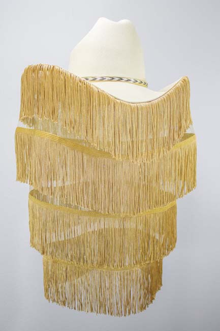A white cowboy hat with multiple layers of gold fringe hanging from it.