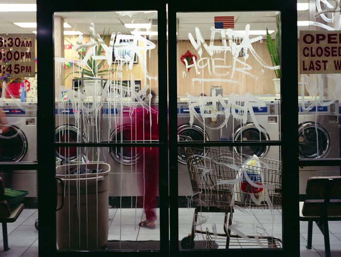 View of a laundromat, with acid etch graffiti on the glass doors.