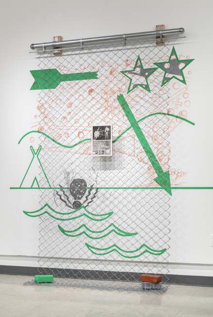 Wall piece with bright green infographic-style markings, such as arrows, stars, and a rudimentary landscape, with a panel of chain link suspended in front of it.