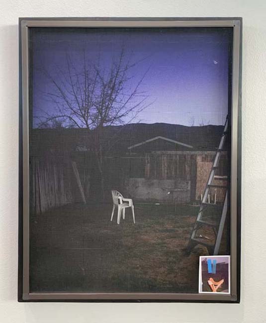 A single white plastic chair in the middle of a darkened backyard at twilight.