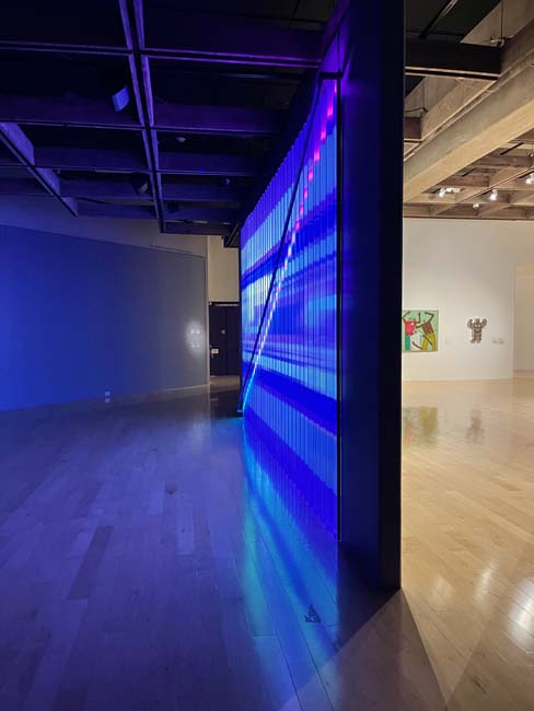 Installation view showing a side view of a video installation of bright blue and red patterns.