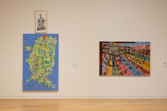 Installation view with two works on the wall, on the left a map in green and blue, and on the right a multi-colored spiral.