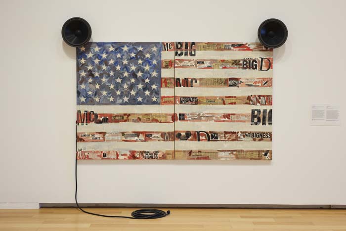 Painting of an American flag with newsprint underneath and two loudspeakers on either side.