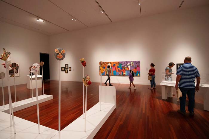 Installation view of an exhibition of Latin art at Colorado College's Fine Art Center, with various luchador masks displayed in the foreground.