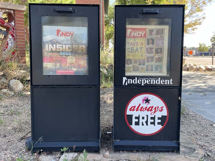 Two black newsstands with copies of the Colorado Springs Indy, with a sign on one that reads "Always Free."