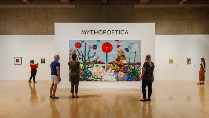 Installation view of Mythopoetica at the Palm Springs Art Museum, with a large-scale desert landscape with oversized flowers in the center.