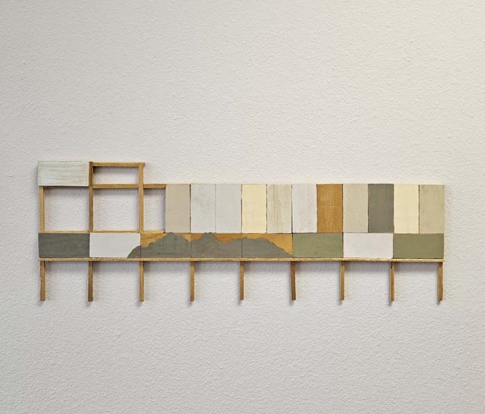 A long wall-mounted, model-scale mixed media artwork that resembles a weathered billboard frame.