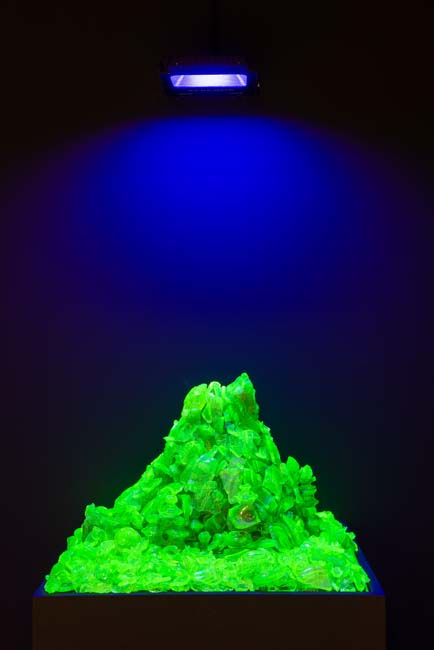 A pile of antique glass colored with depleted uranium, lit from above and glowing bright green.