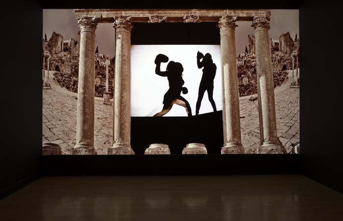 Still of a video with two shadow boxers on a screen, with corinthian columns framing it.