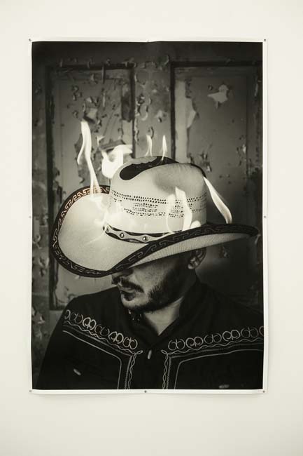 A black and white photograph of a man wearing a cowboy hat that is on fire.