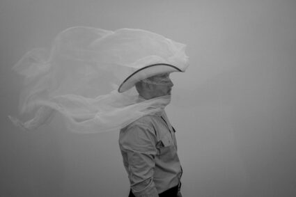 Video still of José Villalobos wearing a cowboy hat covered in white mesh that continuously, diaphanously blows in the breeze.