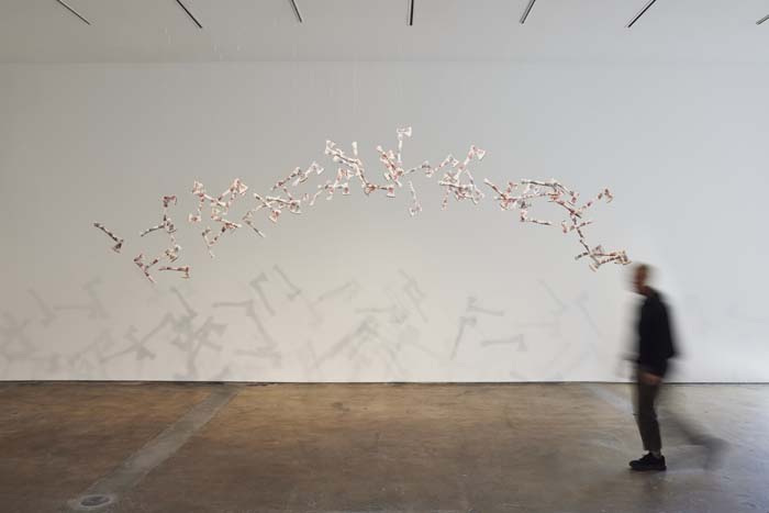 A group of 60 white porcelain hatchets suspended from the ceiling by transparent threads in an arc.