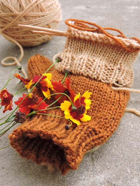 A small bundle of coreopsis flowers resting on an in-process crocheted coreopsis-colored mitten.