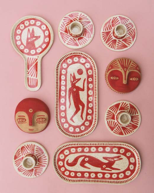 Various red colored ceramics pieces with motifs of coyotes and moons, set on a pink background.