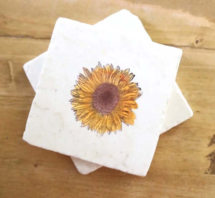 Marble coaster with a sunflower, stacked on another coaster, on a wooden table viewed from above.