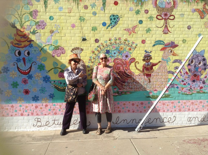 Beatrice Moore (right) and a friend stand in front of Moore's mural Between Innocence and Knowing located on the Kooky Krafts Shop at 1500 Grand Avenue