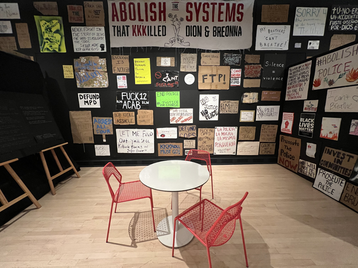 George Floyd exhibition at ASU Art Museum incudes a table and chairs among a display of signs and posters