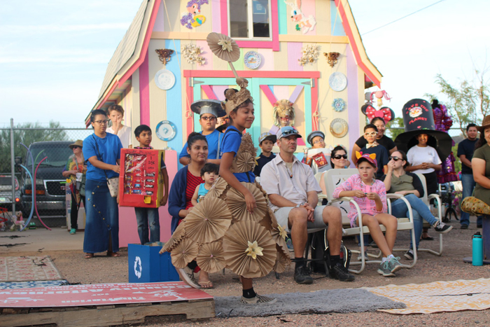 A girl with cardboard swirls participates in the Untrashed Recycled Fashion Show at Weird Garden during the 2019 Grand Avenue Festival in front of a shed decorated by Beatrice Moore
