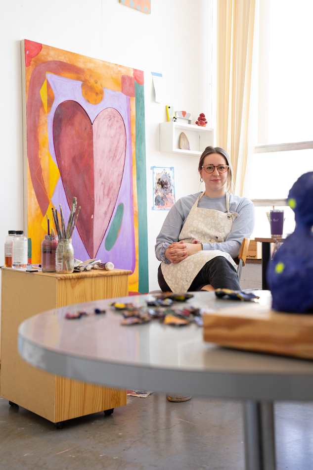 Claire Kennedy in her studio next to a painting of a heart.
