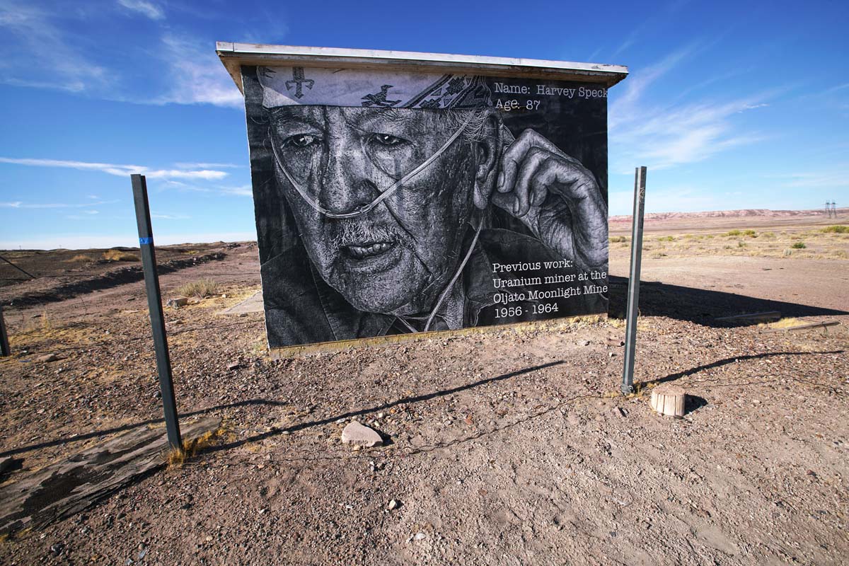A small outbuilding wheatpasted with a black and white photograph of an elderly Navajo man with an oxygen tube.