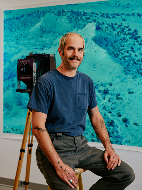 A portrait of David Benjamin Sherry with a blue photograph and camera behind him.