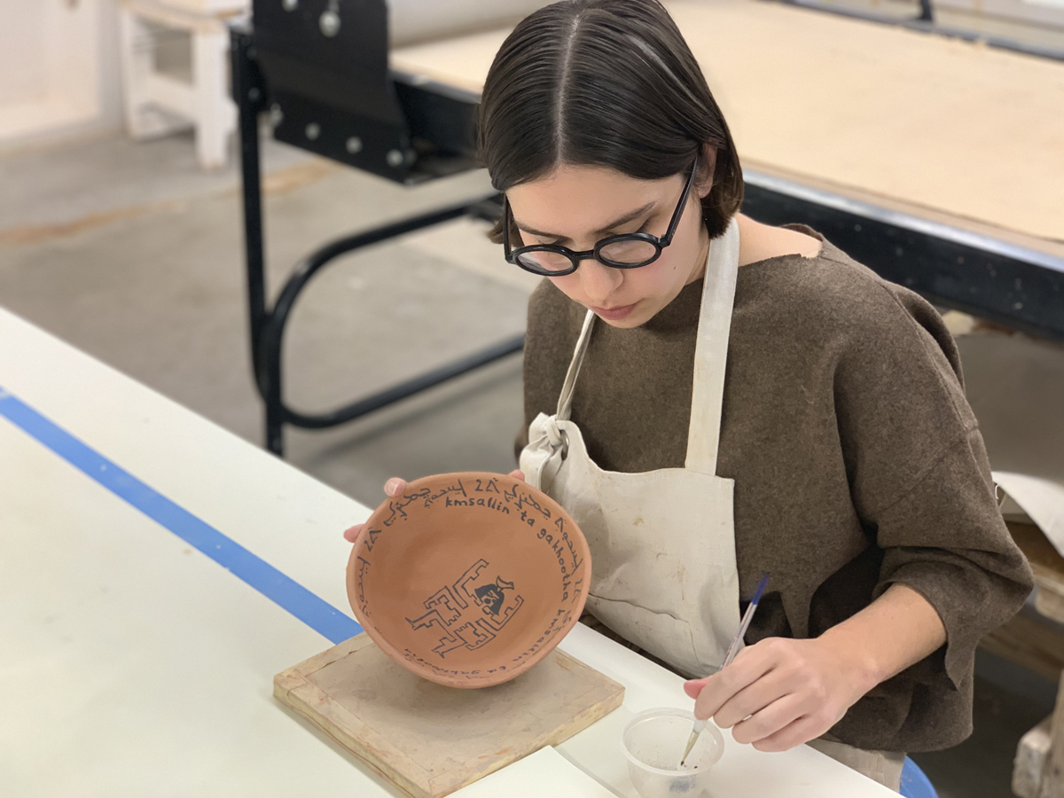 Esther Elia painting black script onto a clay prayer bowl for the workshop she hosted in Arizona.