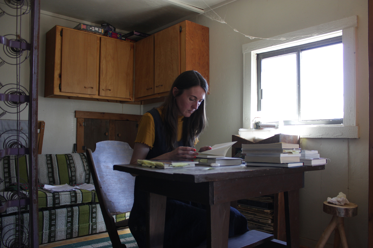 Emma Kemp reading at a desk inside the renovated cabin at Home of Truth. Photography by Emily Arntsen.
