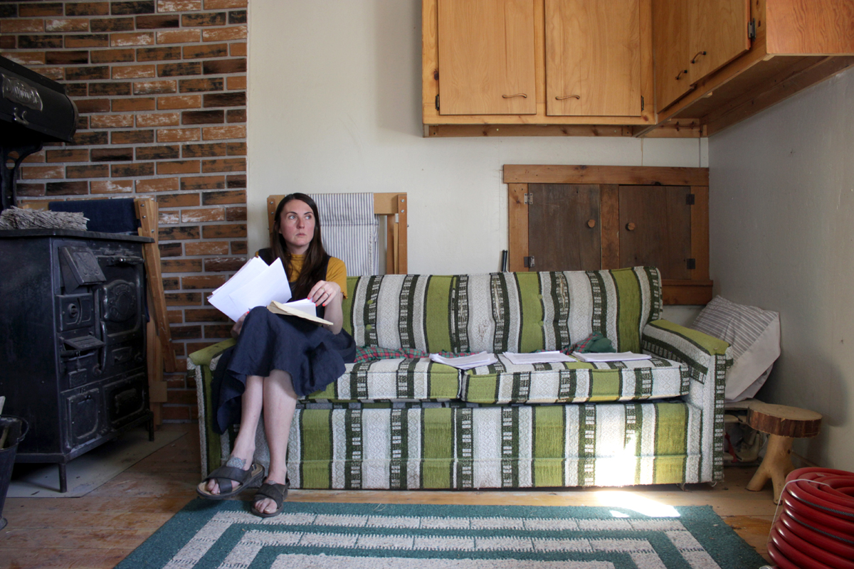Emma Kemp sits on a couch in a renovated cabin at the Home of Truth in Dry Valley, Utah, where she has been writing a book for nearly a decade. Photography by Emily Arntsen.