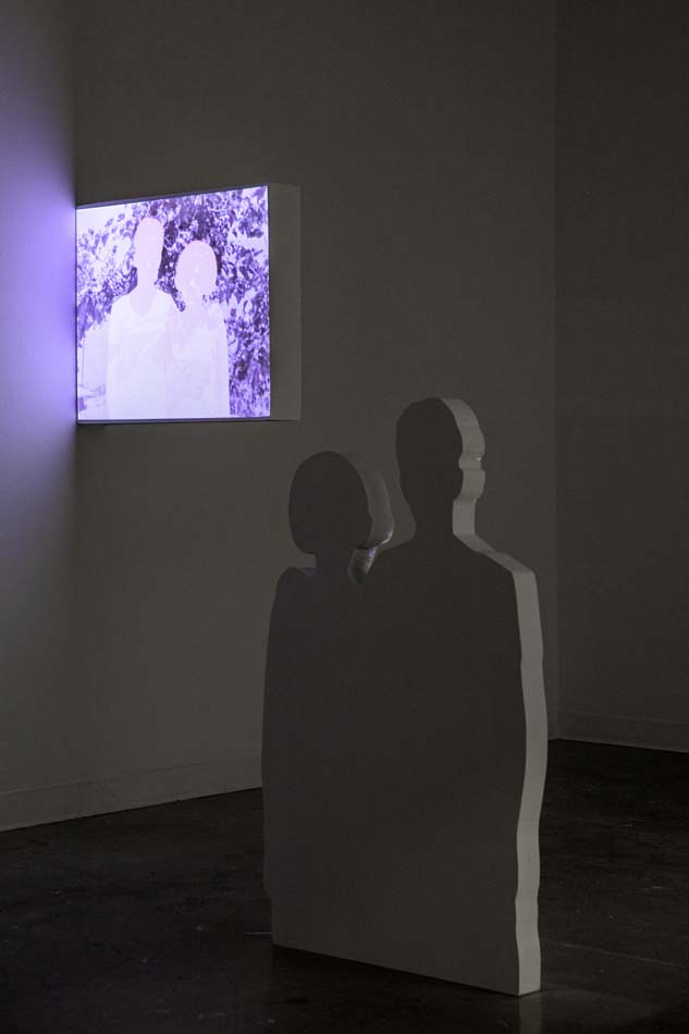 An artwork by Andrew Ina, with a free-standing silhouette cut out of the figures of two women, next to a video projected on a panel emerging from the wall.