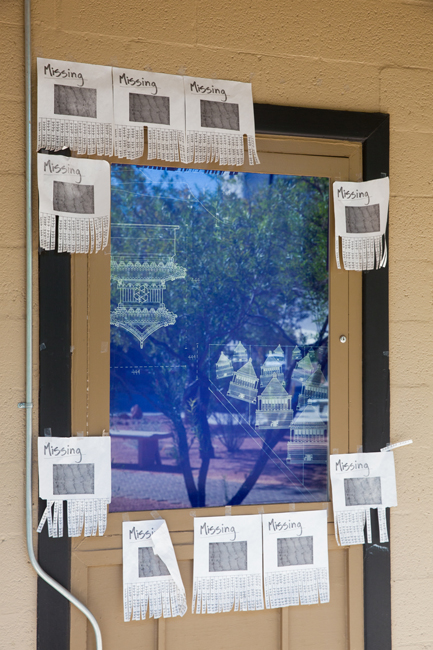 A side view of Tailings by Jeannie Hua shows architectural renderings on a window and sheets of printed paper 